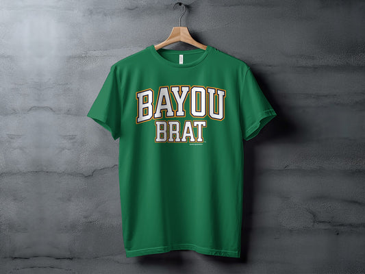 Green t-shirt with white and gold text reading "BAYOU BRAT" on a hanger.