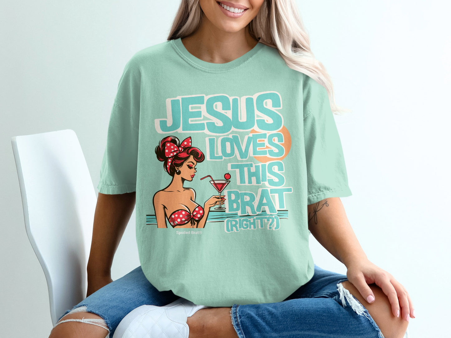 Light teal t-shirt with a cartoon pin-up girl and text "JESUS LOVES THIS BRAT (RIGHT?)".