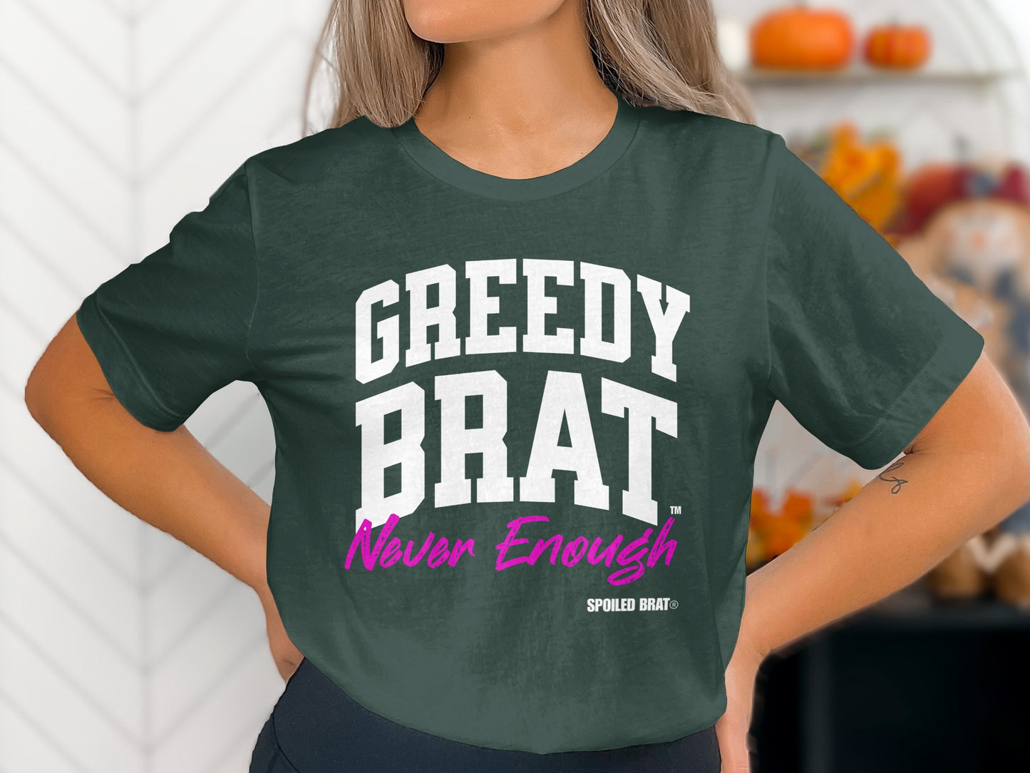 Dark green t-shirt with white "GREEDY BRAT" and pink "Never Enough" text.