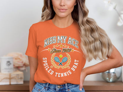 Orange t-shirt with "Kiss My Ace Spoiled Tennis Brat" graphic.