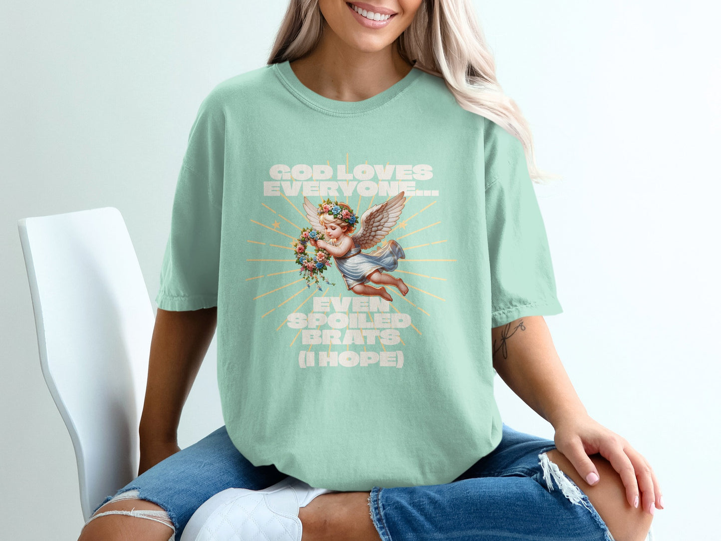 Mint green t-shirt with angelic cherub graphic and text "God loves everyone... even spoiled brats (I hope)".