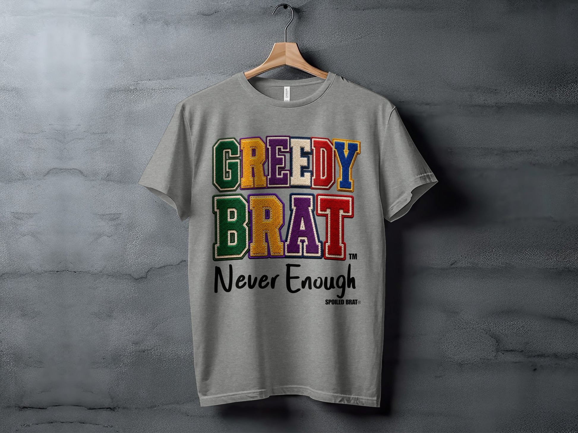 Grey t-shirt with "GREEDY BRAT Never Enough" text in embroidered letters.