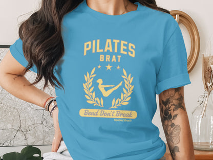 Turquoise t-shirt with "PILATES BRAT Bend Don't Break" text and laurel wreath graphic.