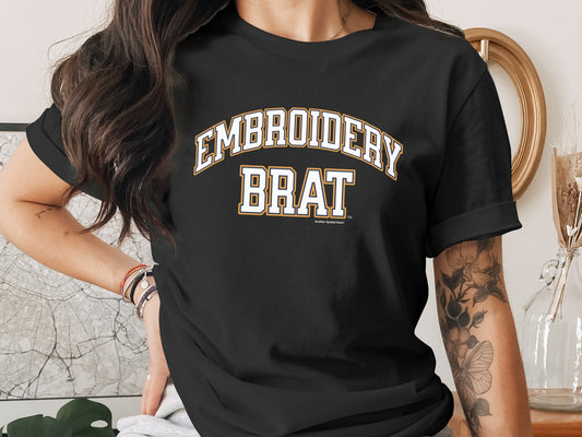 Black t-shirt with white and gold "EMBROIDERY BRAT" text.
