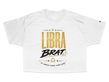 White cropped t-shirt featuring "LIBRA BRAT" in gold and black with Libra symbol and descriptive words.