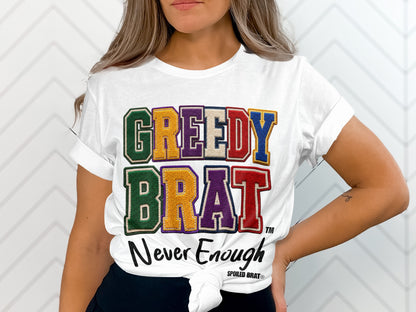 White t-shirt with embroidered "GREEDY BRAT" and "Never Enough" text.