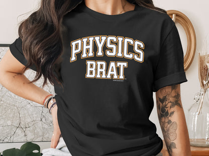 A person wears a black crewneck t-shirt with the words PHYSICS BRAT printed across the chest.