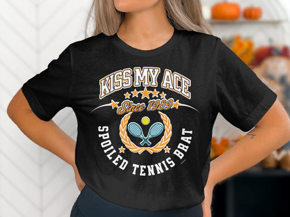 Black t-shirt with "Kiss My Ace Since 1989 Spoiled Tennis Brat" text and tennis graphic.