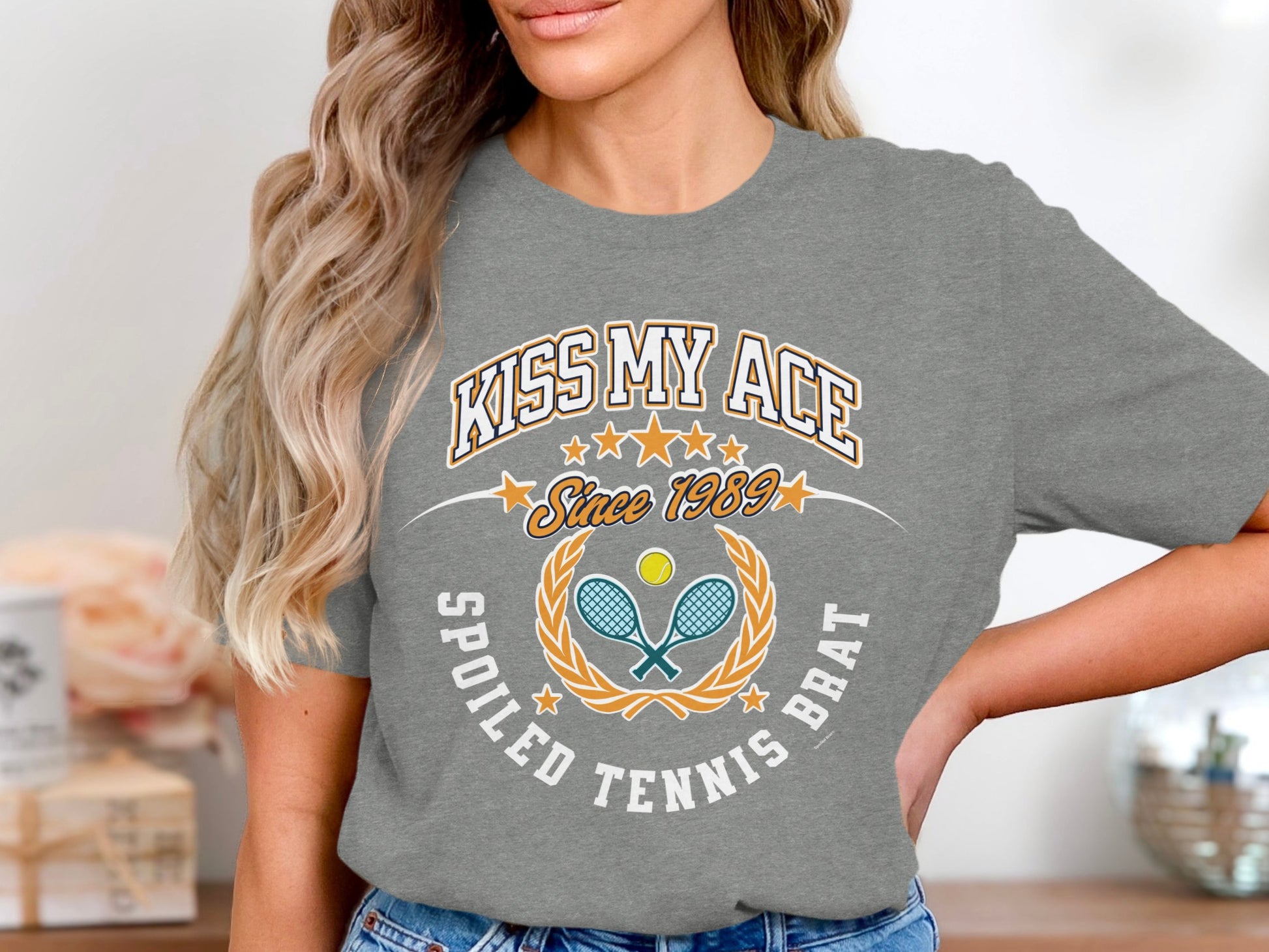 "Kiss My Ace Spoiled Tennis Brat" graphic tee with tennis racket and ball design.