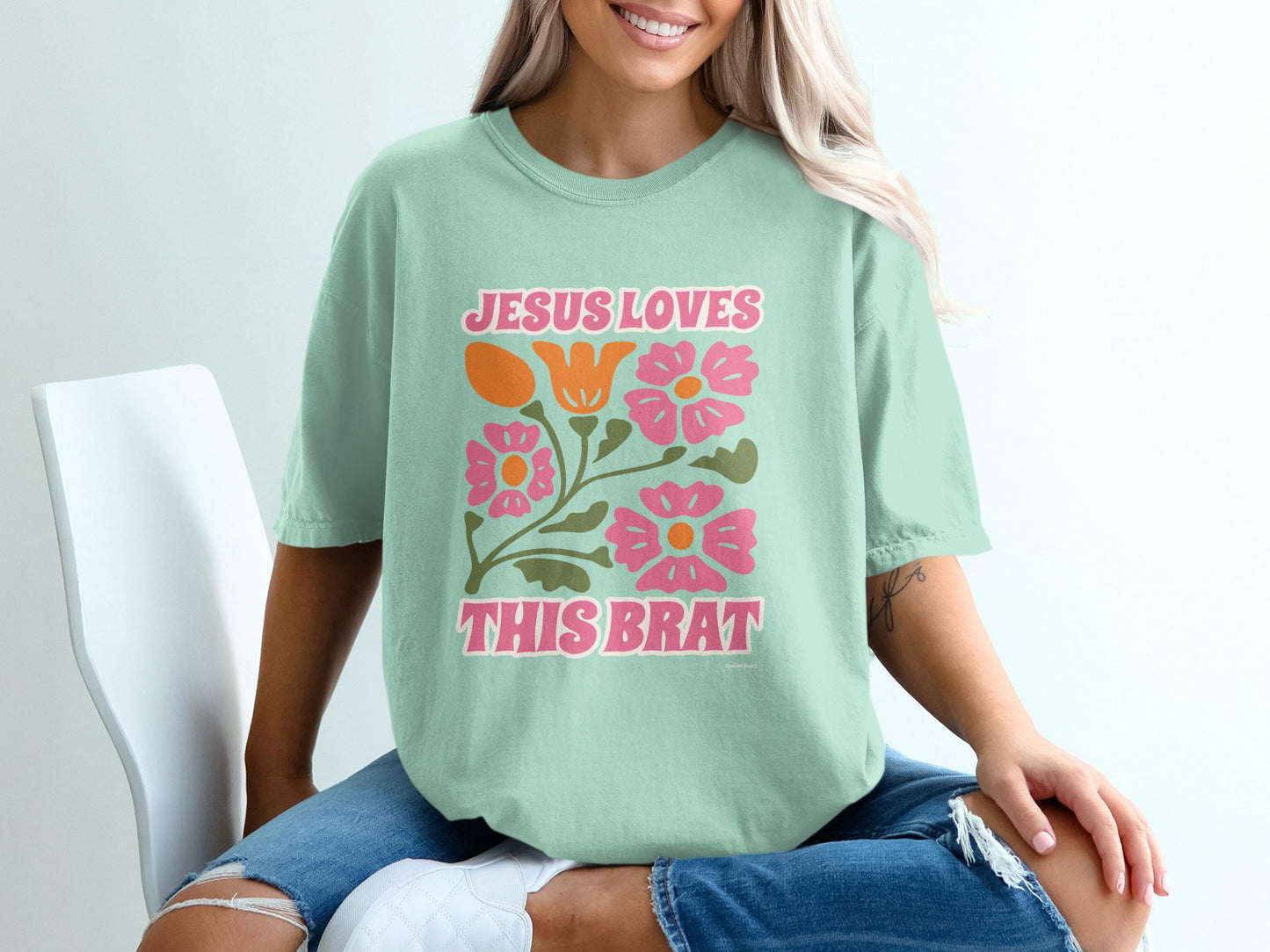 Mint t-shirt with "Jesus Loves This Brat" in pink and orange with floral accents.