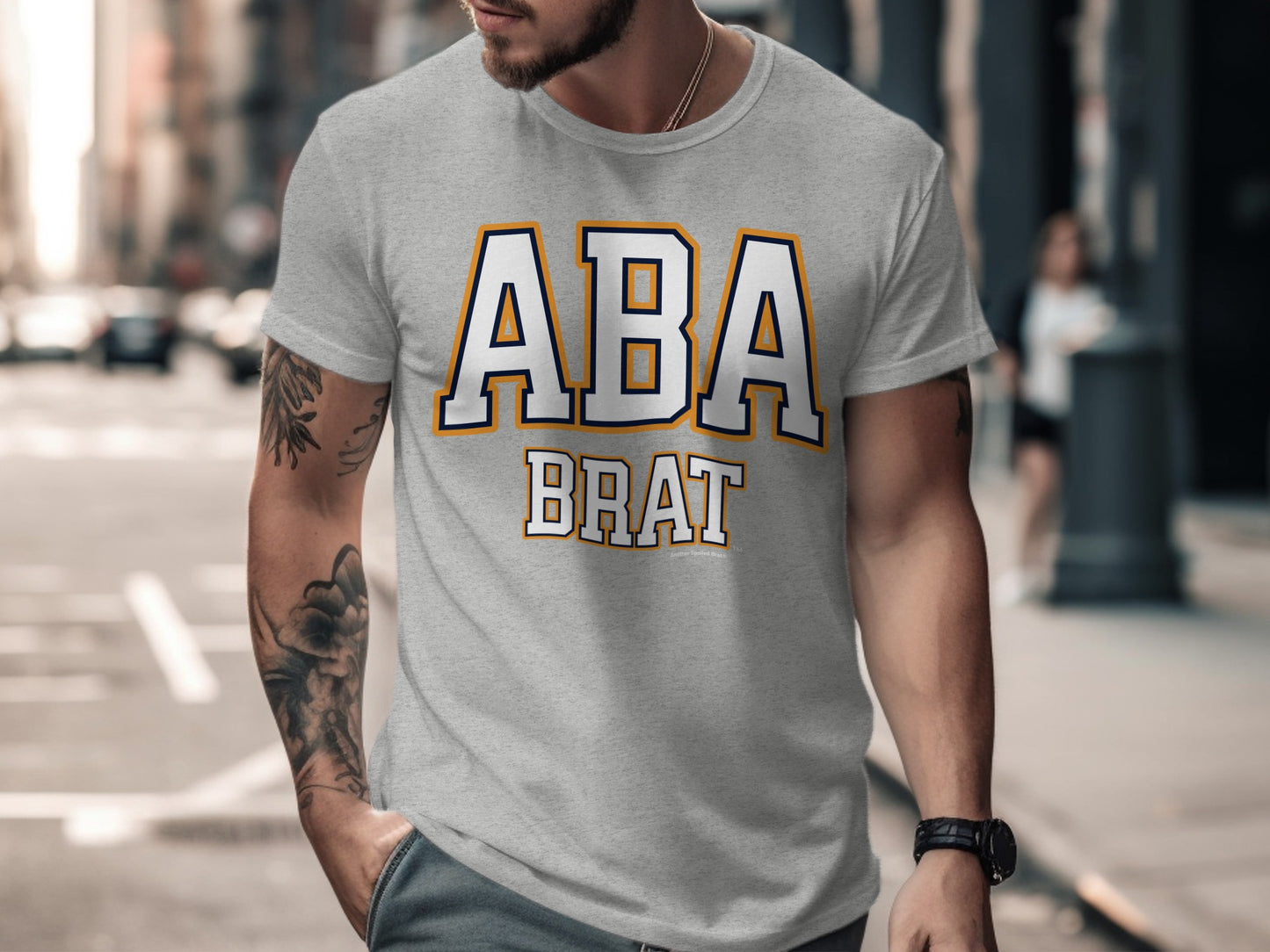Grey t-shirt with "ABA BRAT" text in white block letters with blue and orange outline.
