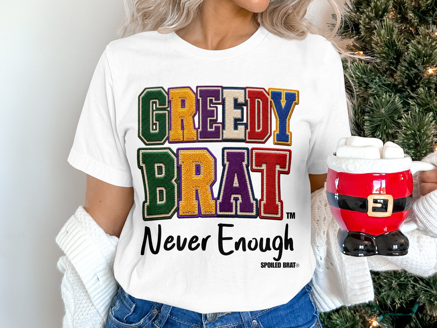 White t-shirt with "GREEDY BRAT Never Enough" text in colorful varsity letters.