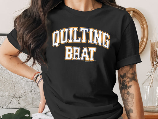 Black t-shirt with white text "QUILTING BRAT" in collegiate style lettering.