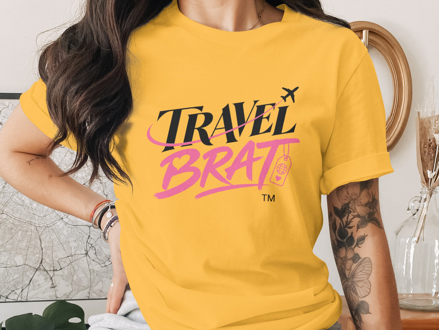 Yellow T-shirt with "TRAVEL BRAT" in black and pink text, airplane, and passport icon.