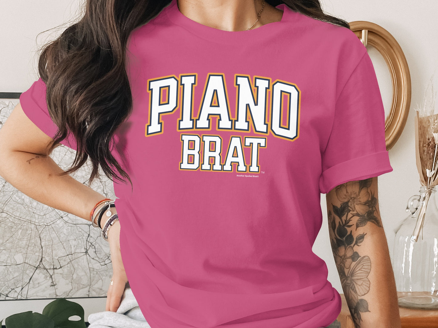 Pink t-shirt with "PIANO BRAT" text in collegiate-style lettering.