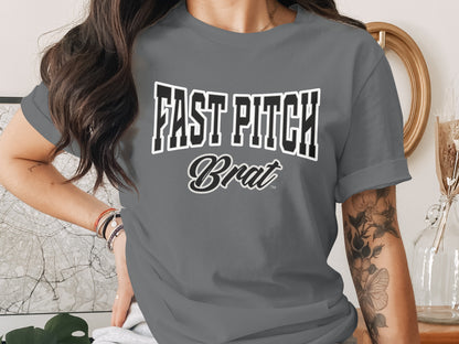 "Fast Pitch Brat" text on a grey t-shirt worn by a woman with tattoos.