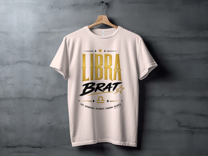 White t-shirt with gold "LIBRA BRAT" text, zodiac symbol, and descriptive words.