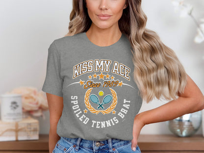 Grey t-shirt with "Kiss My Ace Since 1989 Spoiled Tennis Brat" graphic.