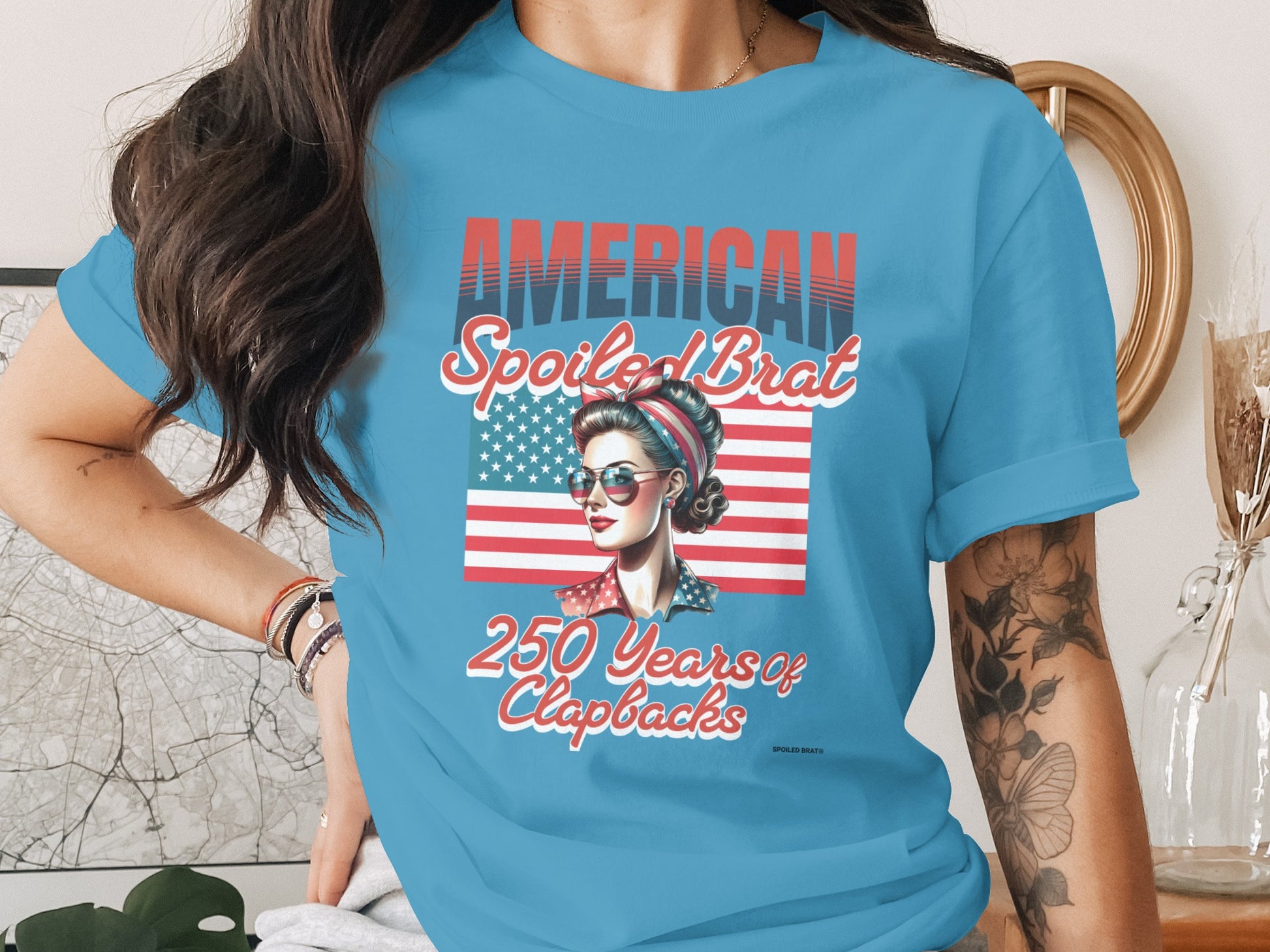 Light blue t-shirt with "AMERICAN SPOILED BRAT" text and a retro woman.