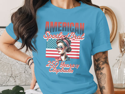 Light blue t-shirt with "AMERICAN SPOILED BRAT" text and a retro woman.