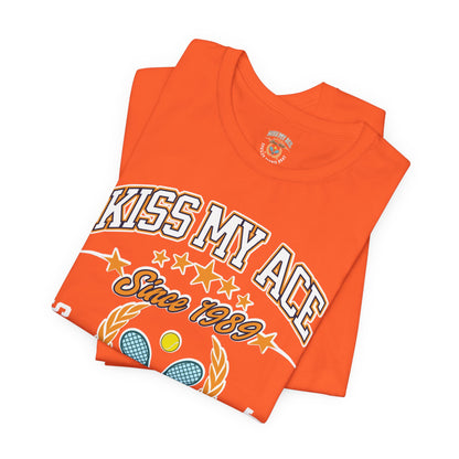 Orange t-shirt with "Kiss My Ace Since 1989" text and tennis graphics.