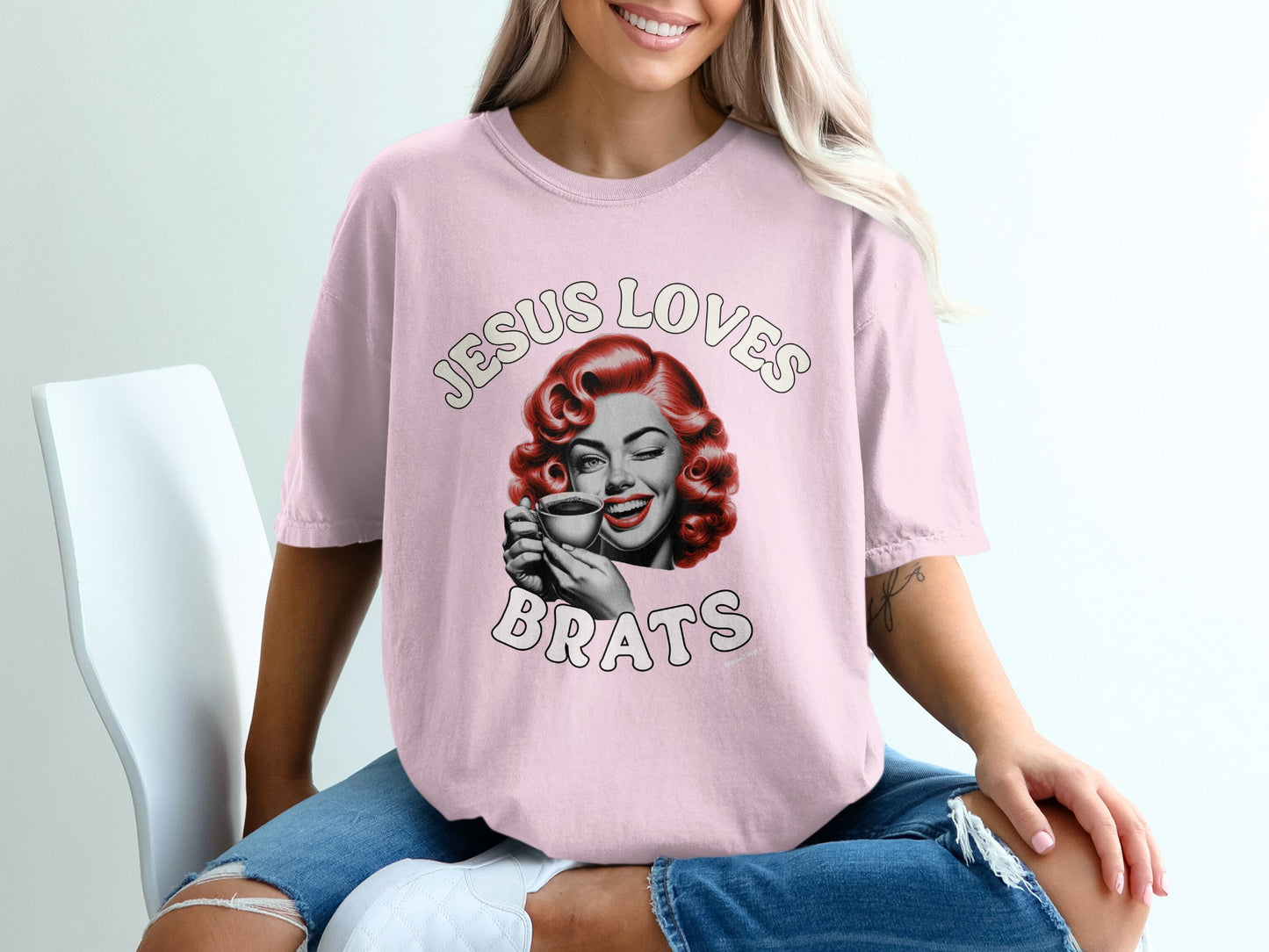 Pink t-shirt with retro woman winking and holding coffee, text "Jesus Loves Brats".