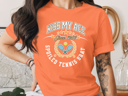Orange t-shirt with "Kiss My Ace Spoiled Tennis Brat" text and tennis graphics.