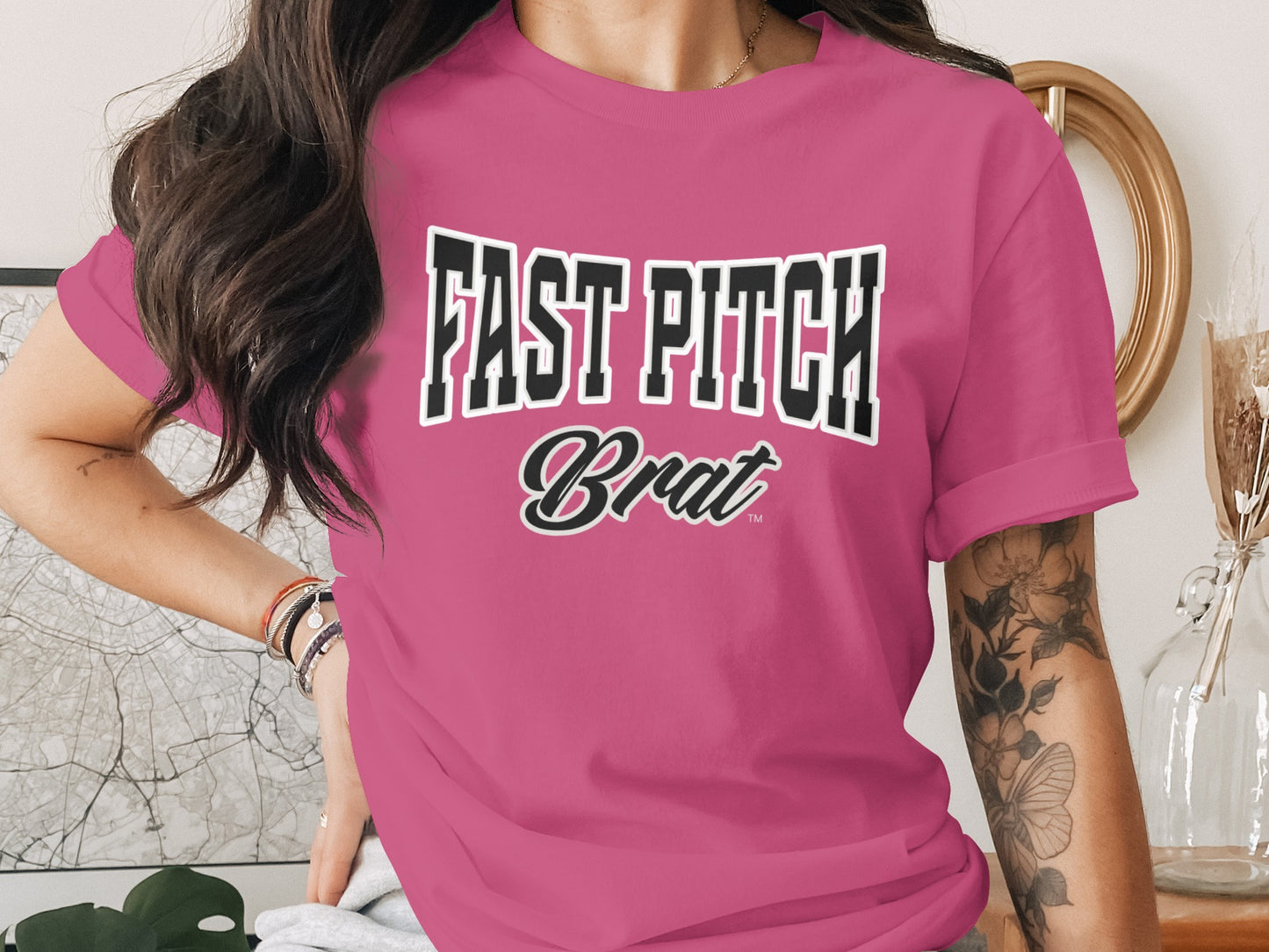 Pink t-shirt with "FAST PITCH Brat" text and tattoo on arm.