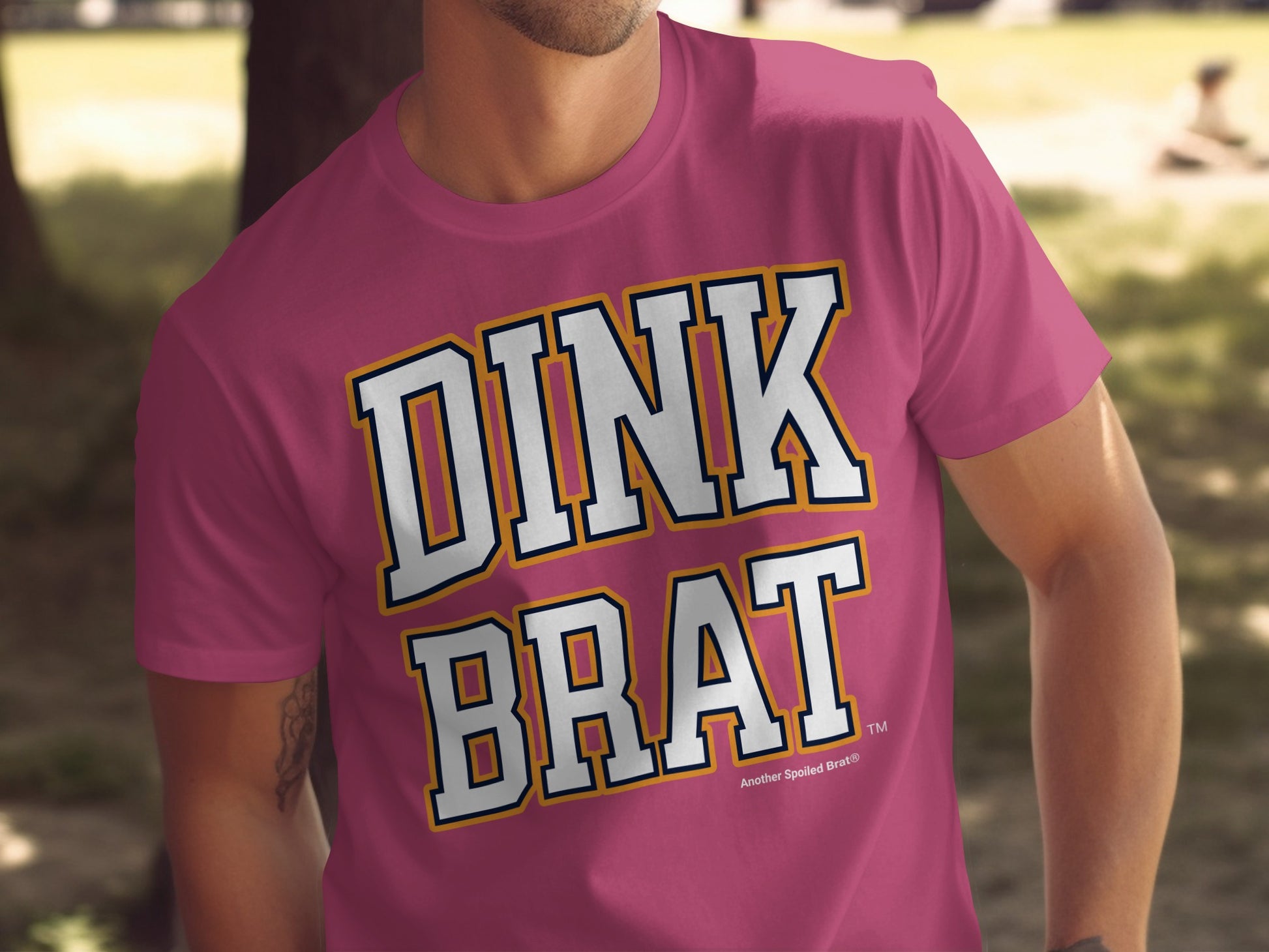 Pink t-shirt with "DINK BRAT" text in white, navy, and yellow lettering.