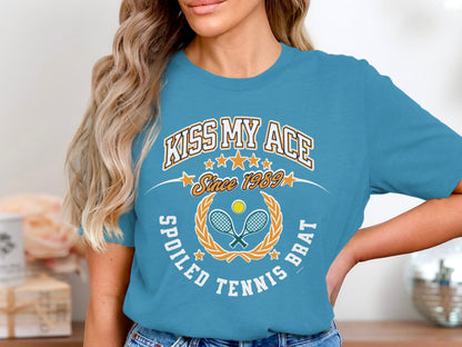 Blue t-shirt with "Kiss My Ace Since 1989 Spoiled Tennis Brat" text and crossed racquets.