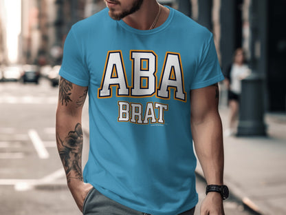 Turquoise t-shirt with "ABA BRAT" text, city street background.