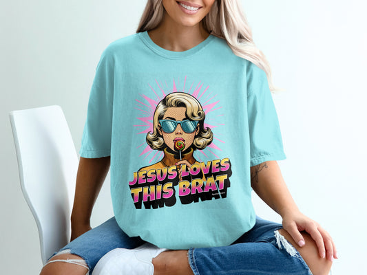Light blue t-shirt with "Jesus loves this brat" graphic and retro woman with lollipop.
