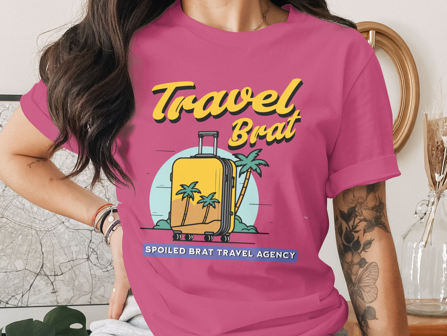 Pink t-shirt with yellow text "Travel Brat" and a yellow suitcase with palm trees.