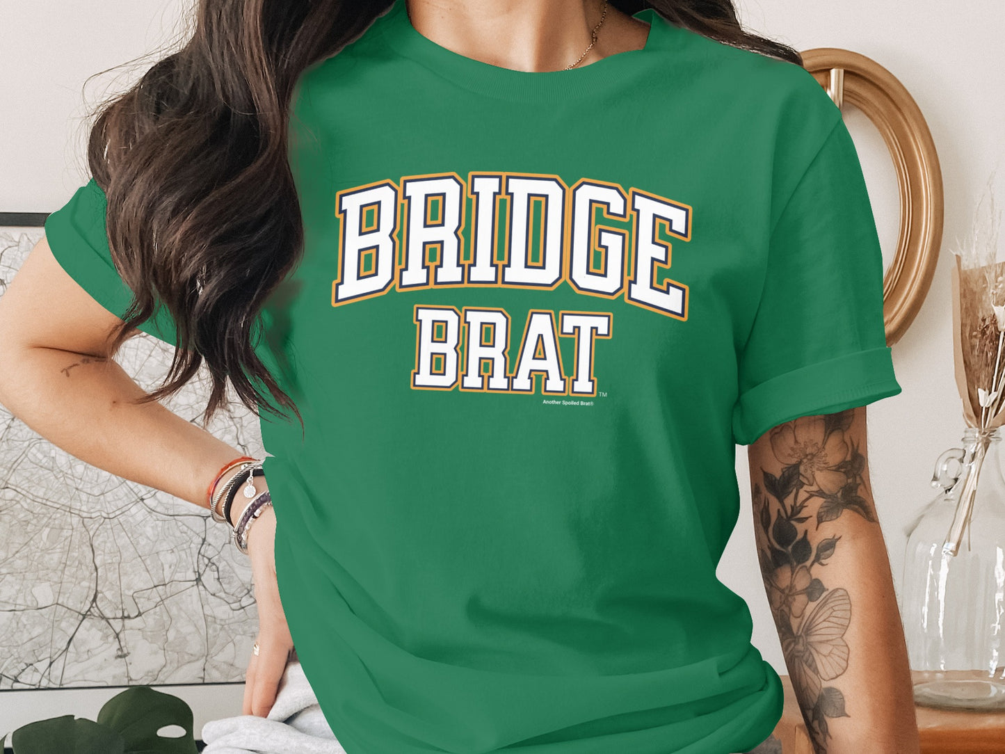 Green t-shirt with white lettering that reads "BRIDGE BRAT"