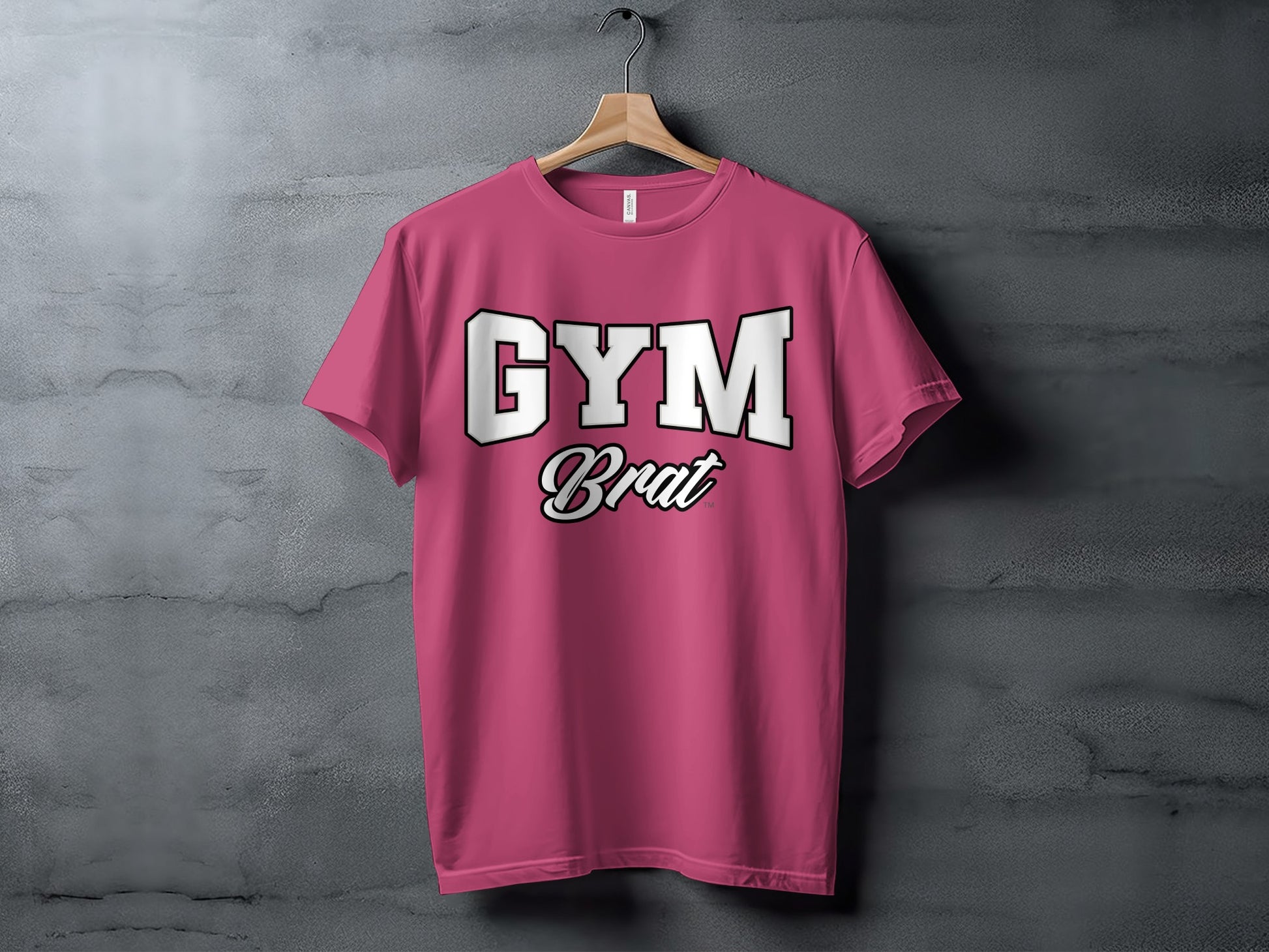 Pink t-shirt with "GYM Brat" text on a gray concrete background.