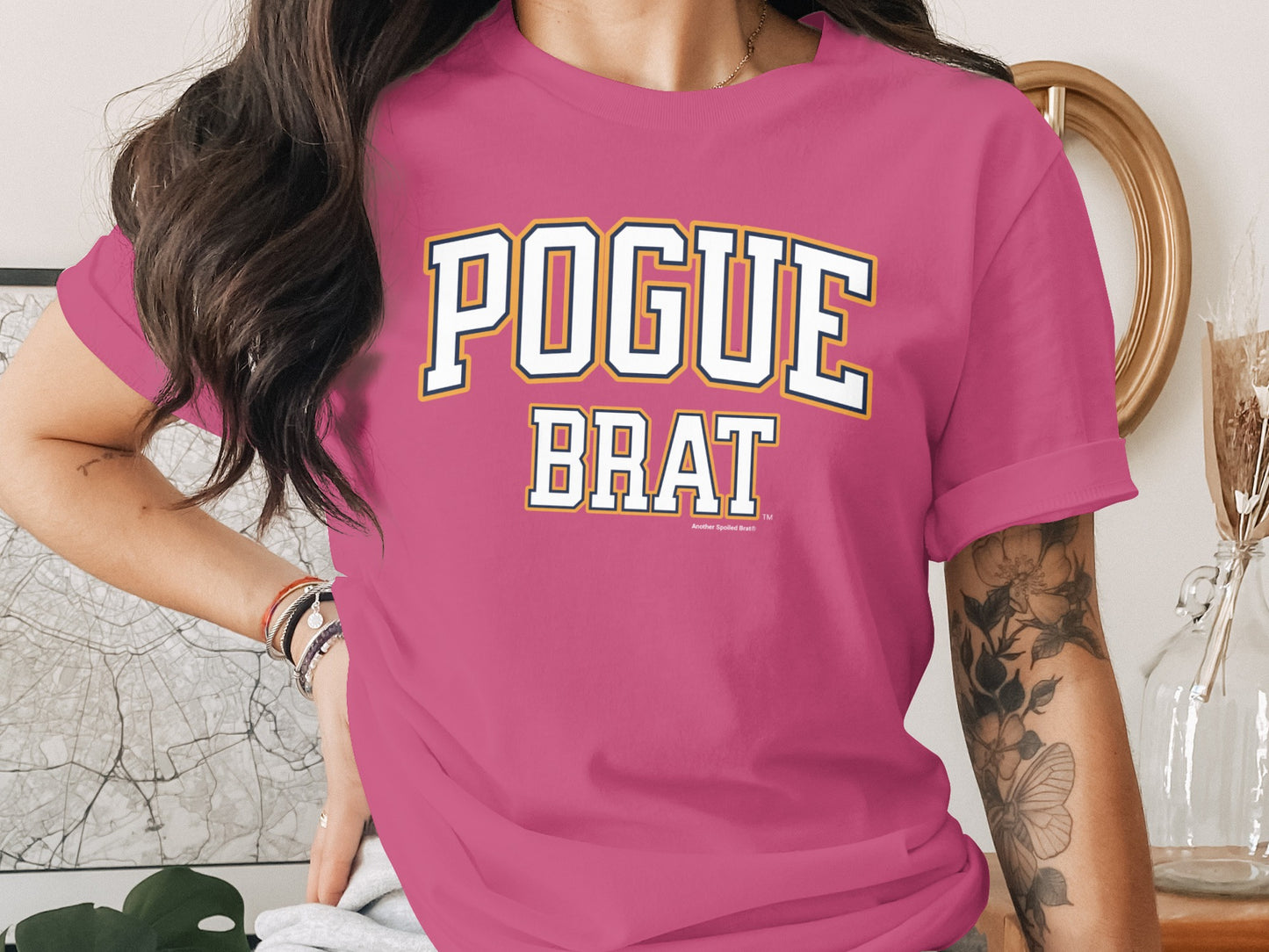 Pink t-shirt with white and yellow text that reads "POGUE BRAT."
