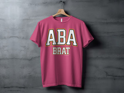 Pink t-shirt hanging on a wooden hanger, with "ABA BRAT" text.