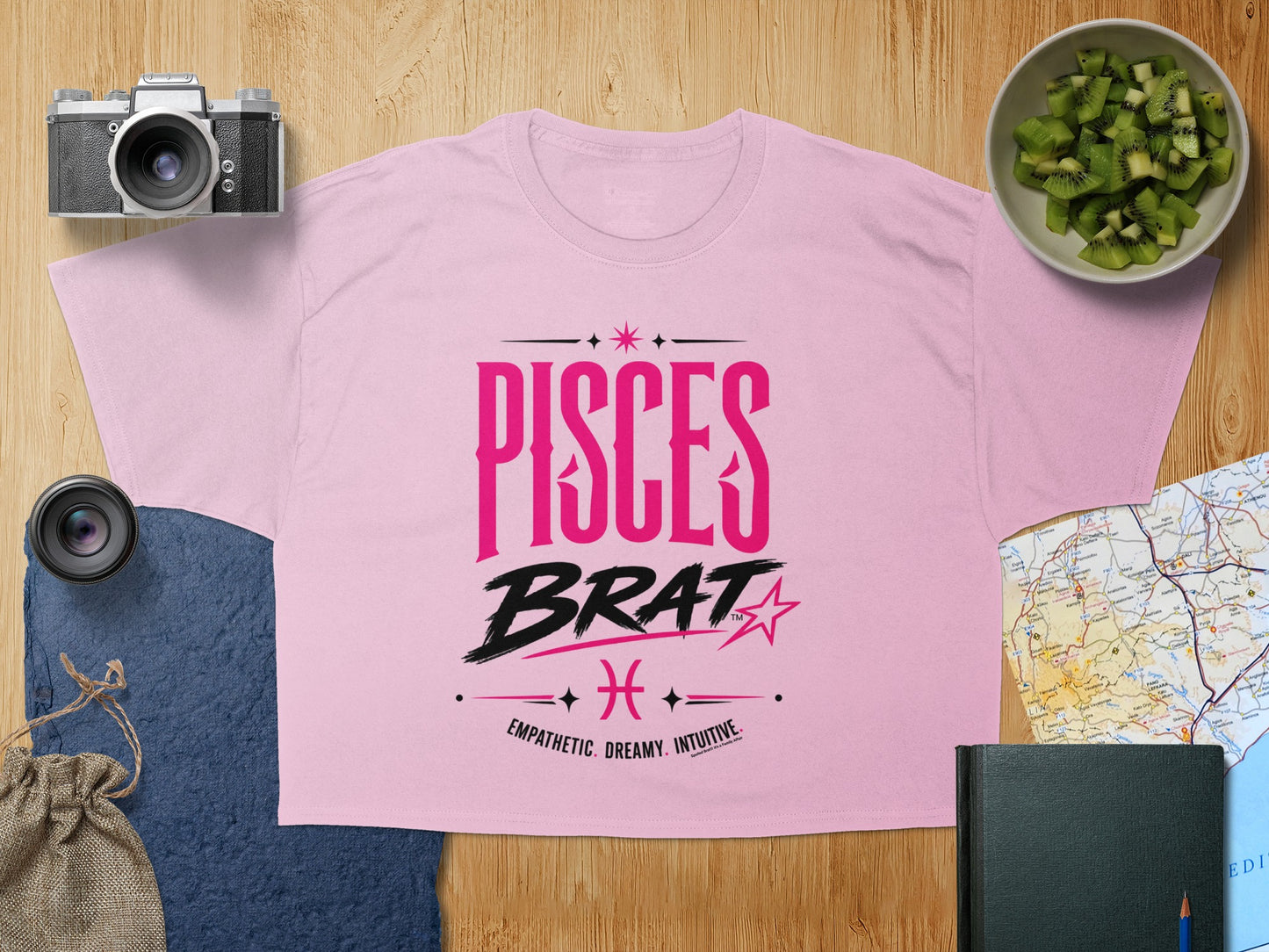 Pink t-shirt with bold "PISCES BRAT" text and traits: empathetic, dreamy, intuitive.