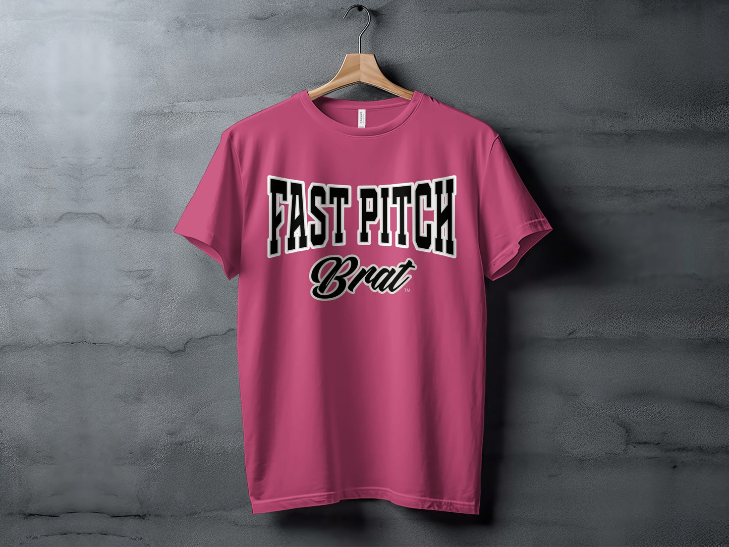 Pink t-shirt with black and white "FAST PITCH Brat" text on a hanger.