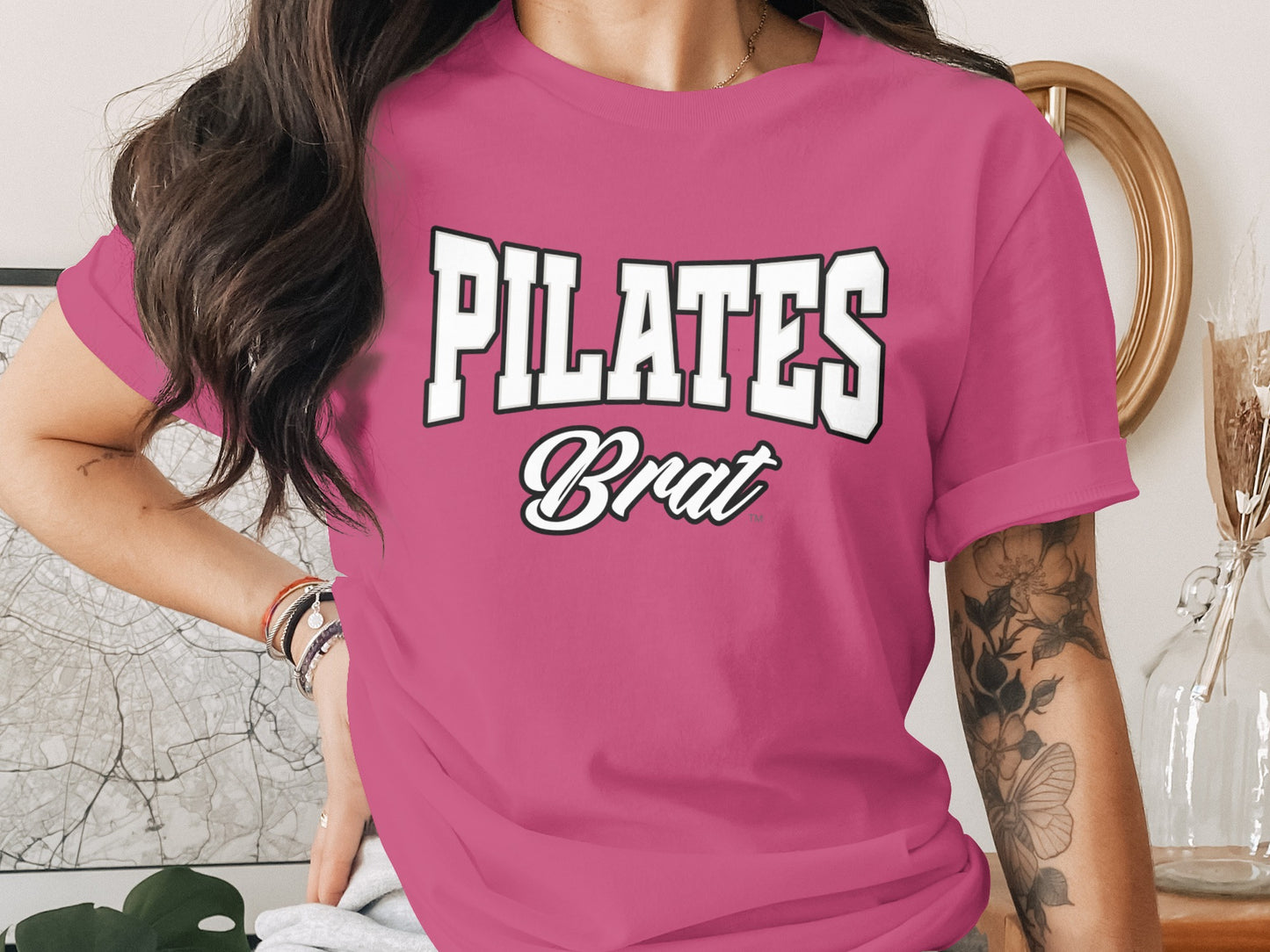 Pink t-shirt with white text "PILATES Brat" in varsity font.