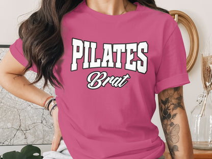 Pink t-shirt with white text "PILATES Brat" in varsity font.