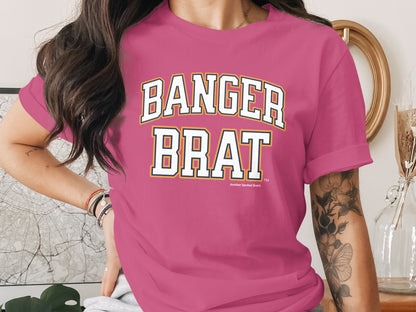 Pink t-shirt with white, yellow, and navy text reading "BANGER BRAT".
