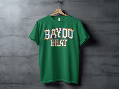 Green t-shirt with white and gold text reading "BAYOU BRAT" on a hanger.
