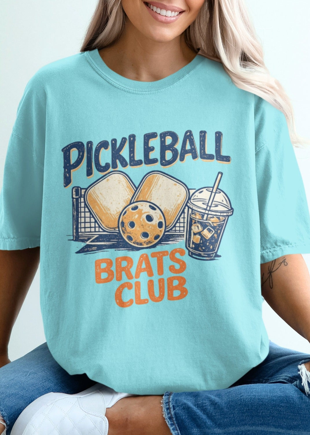 Turquoise t-shirt with "Pickleball Brats Club" graphic and pickleball gear.