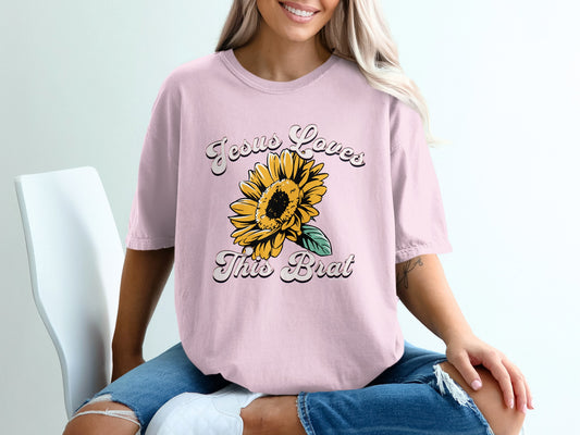 Pink t-shirt with "Jesus Loves This Brat" text and a sunflower graphic.