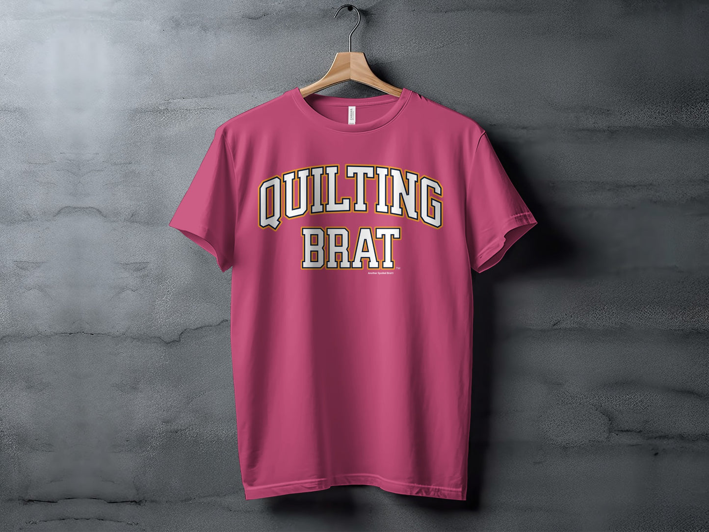 Pink t-shirt with "QUILTING BRAT" in white and gold collegiate lettering.