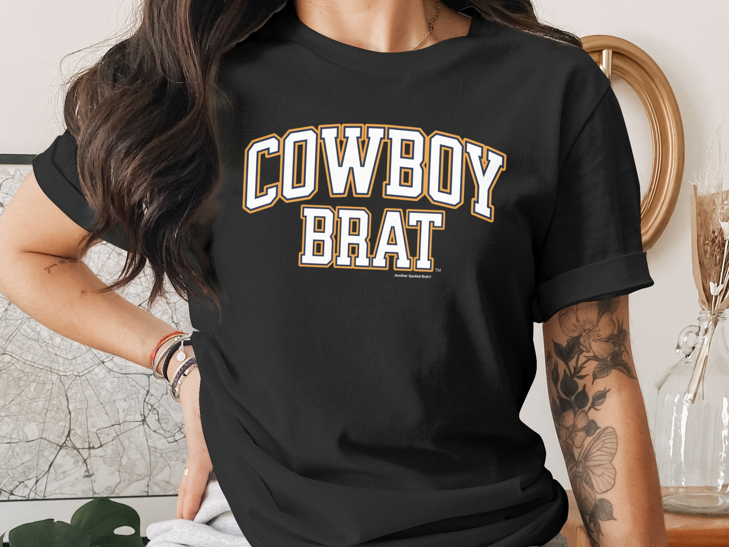 Black t-shirt with "COWBOY BRAT" arched text in yellow and white collegiate font.