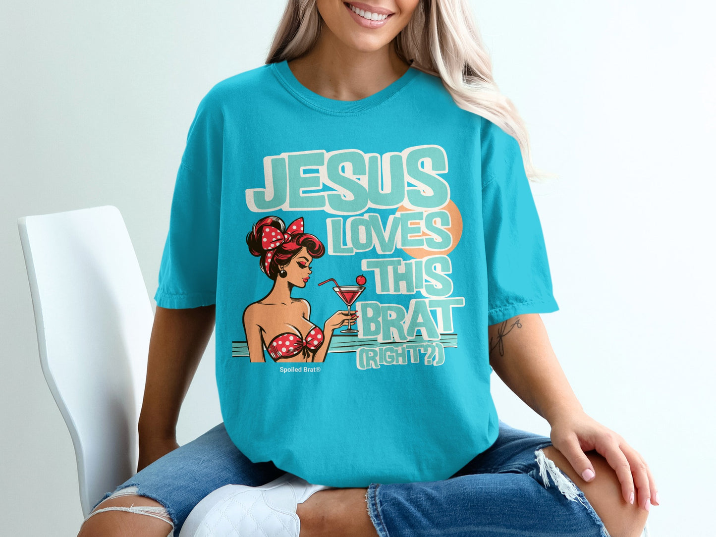 Teal t-shirt with pin-up girl graphic and text "JESUS LOVES THIS BRAT (RIGHT?)".