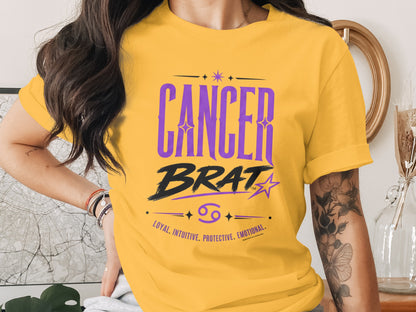 Yellow t-shirt with purple "Cancer Brat" text, zodiac symbol, and descriptors.