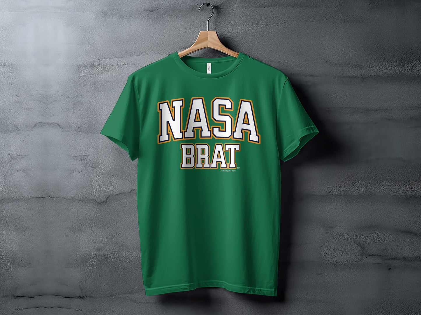Green t-shirt with white and gold "NASA BRAT" text hanging on a wooden hanger.